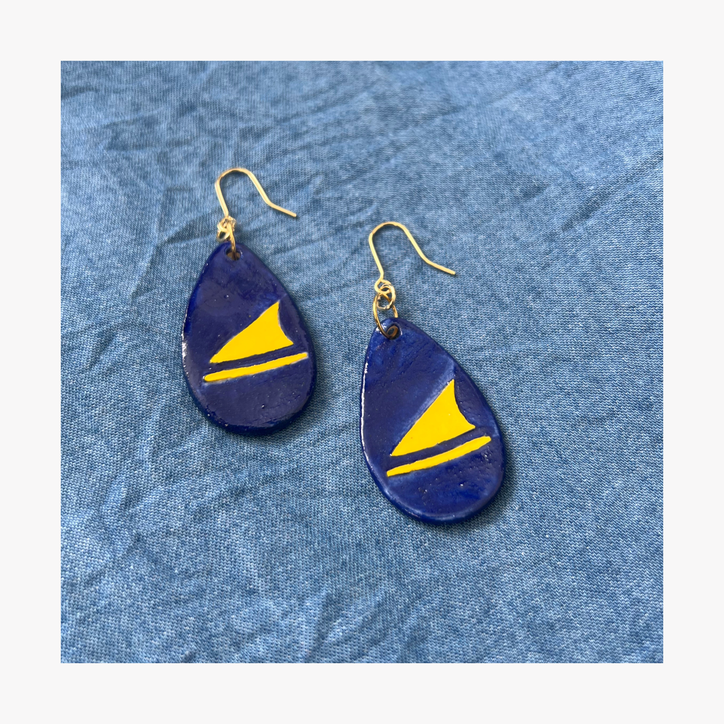 Blue teardrop earrings with yellow triangles that represents boats on a blue textured background