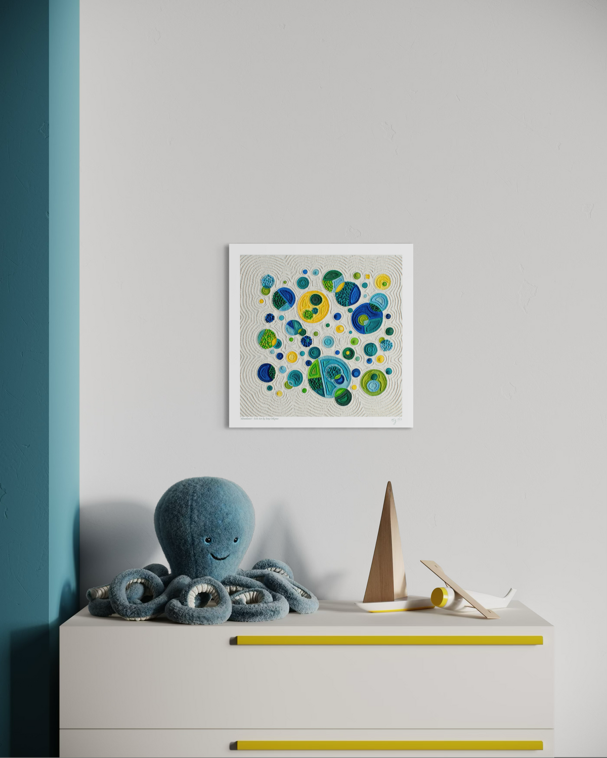 A square fine wall art print called ''Abundance'' originally made with plasticine with colorful bubble-like circles in blue, green, and yellow on a light background, displayed above a white dresser in a styled room with a blue octopus toy and wooden sailboat. Art by Emy Oikawa from Eclo Art.