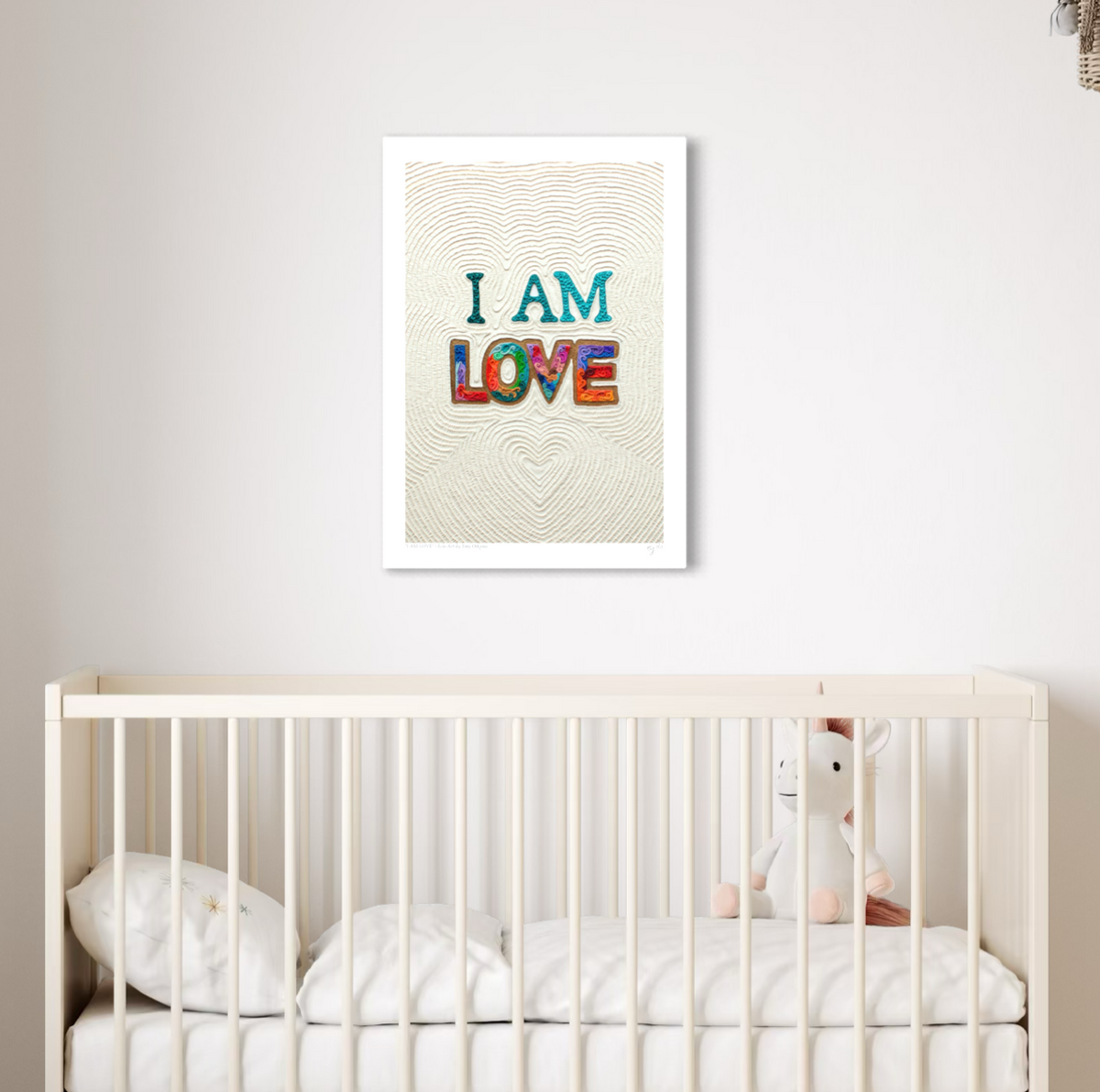 An A3 wall art print with the words 'I AM LOVE' in colorful textured letters hangs above a white crib in a softly lit nursery. Art by New Zealand artist Emy Oikawa from Eclo Art.