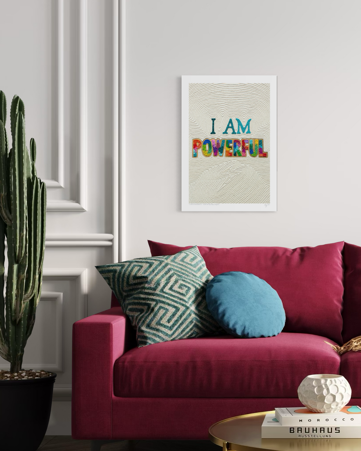 A plasticine clay wall art print with the text 'I AM POWERFUL' hangs on a white wall above a magenta sofa with decorative pillows. Positive and empowering art for everyone!