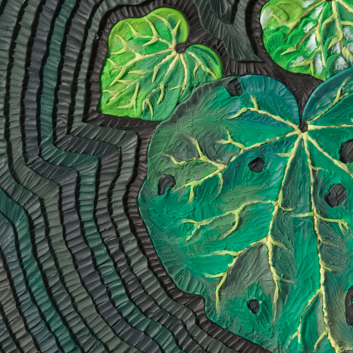 A close-up of a textured decorative surface featuring large green Kawakawa leaf shapes with yellow vein details over a dark wavy background, all originally made with plasticine by clay artist Emy Oikawa from Eclo Art.