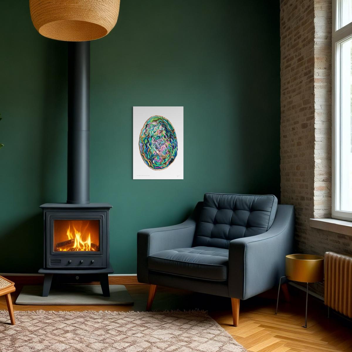 A colorful Paua Shell A3 Art Print hangs on a dark green wall in a modern living room setting with a black wood stove, a gray armchair, and a brick column. Perfect to bring a New Zealand nature piece home. By Emy Oikawa from Eclo Art.