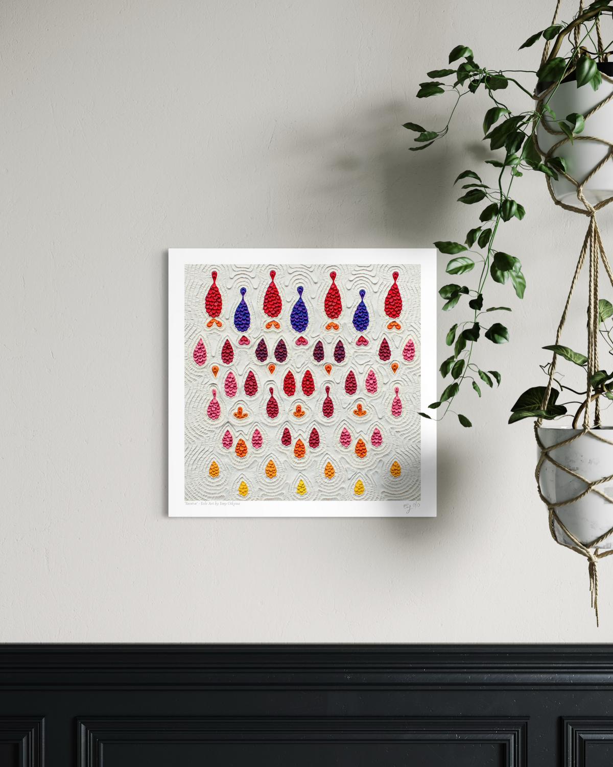 A square wall art print called ''Receive'' featuring rows of colorful hanging teardrop-shaped made with plasticine clay on a light gray background, displayed on a beige wall above a black wainscoted panel with a green hanging plant to the right. Art by New Zealand clay artist Emy Oikawa.