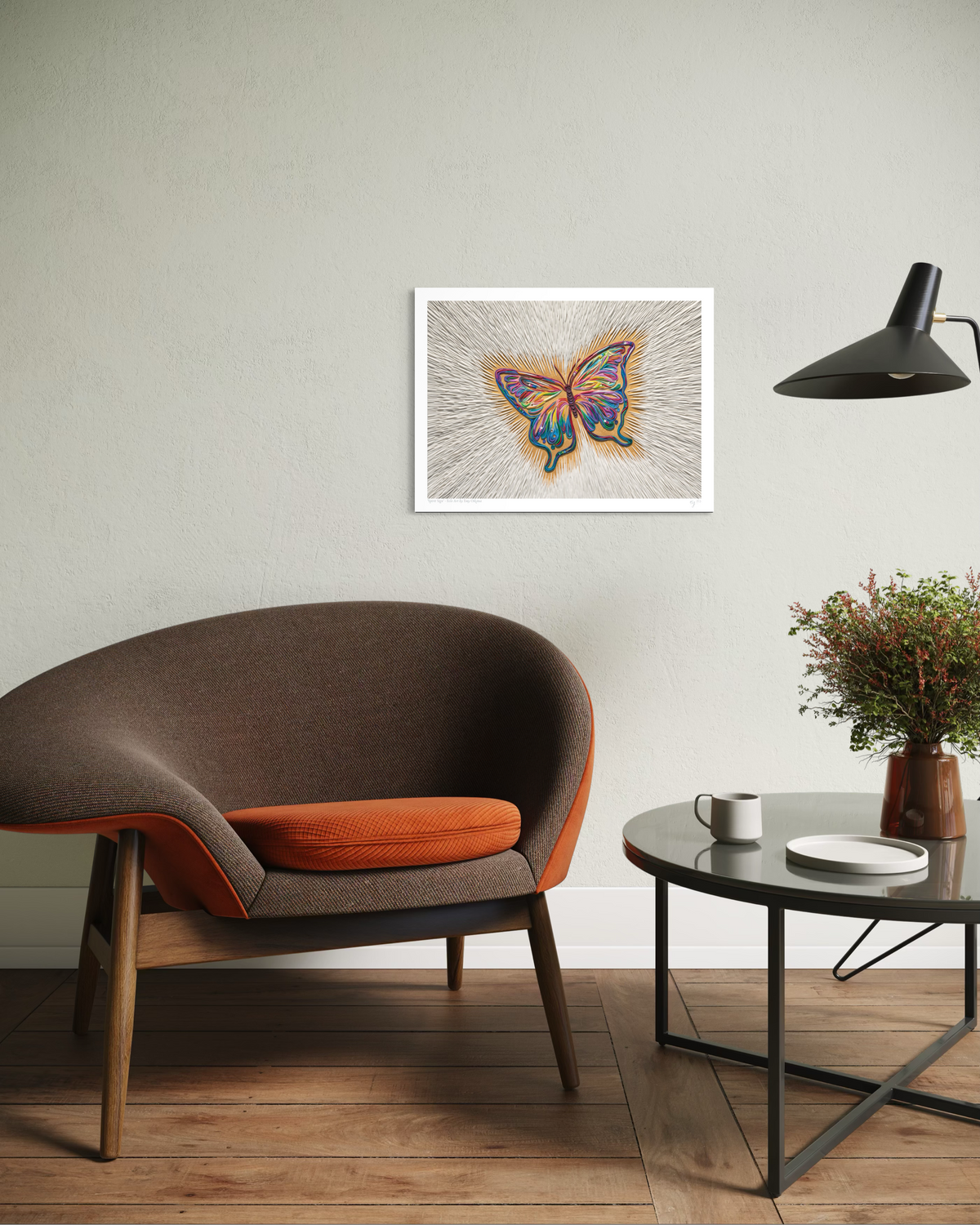 An A3 Print butterfly art called ''Spirit Sign'' by clay artist Emy Oikawa, hangs on a light gray wall in a styled room with a brown armchair, a black side table, a lamp, and a potted plant.