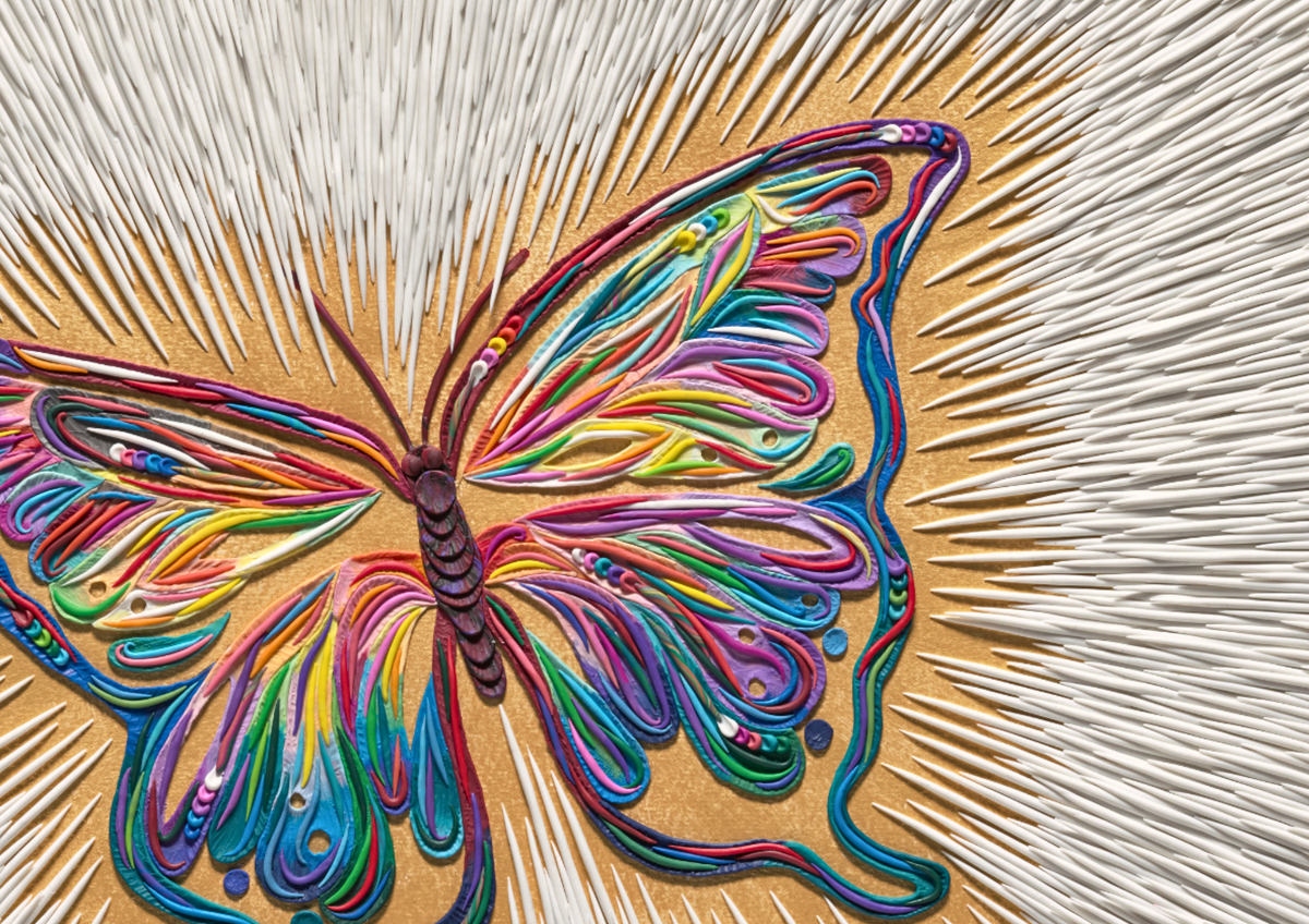 A colorful butterfly artwork close up, called ''Spirit Sign'' with layered, swirling plasticine clay in rainbow hues on a golden acrylic background with radiating white lines.