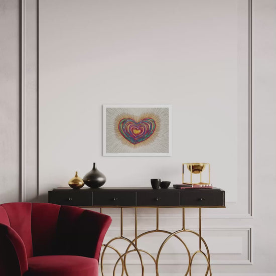 video of the A3 art print featuring a colorful, swirling heart piece called ''Only Love'' hanging on a white paneled wall above a black console table with gold metal legs. A red velvet armchair is visible in the foreground on a checkered floor.