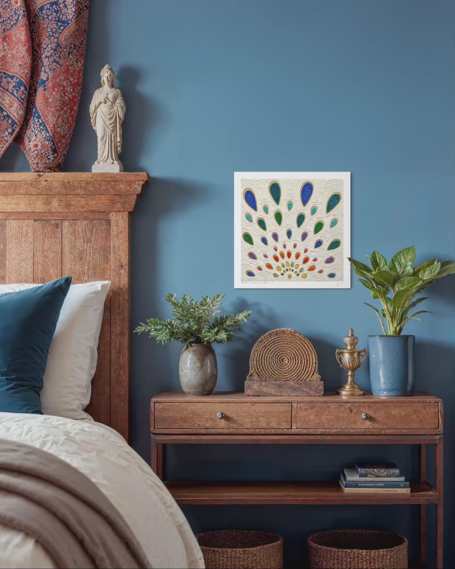A video close up of An abstract art print called ''Growth'' by clay artist Emy Oikawa. A colorful peacock feather-like shapes expanding outwards. The print hangs on a blue wall in a styled bedroom. The scene includes a wooden bed frame, nightstand, plants, woven baskets, and decorative objects.