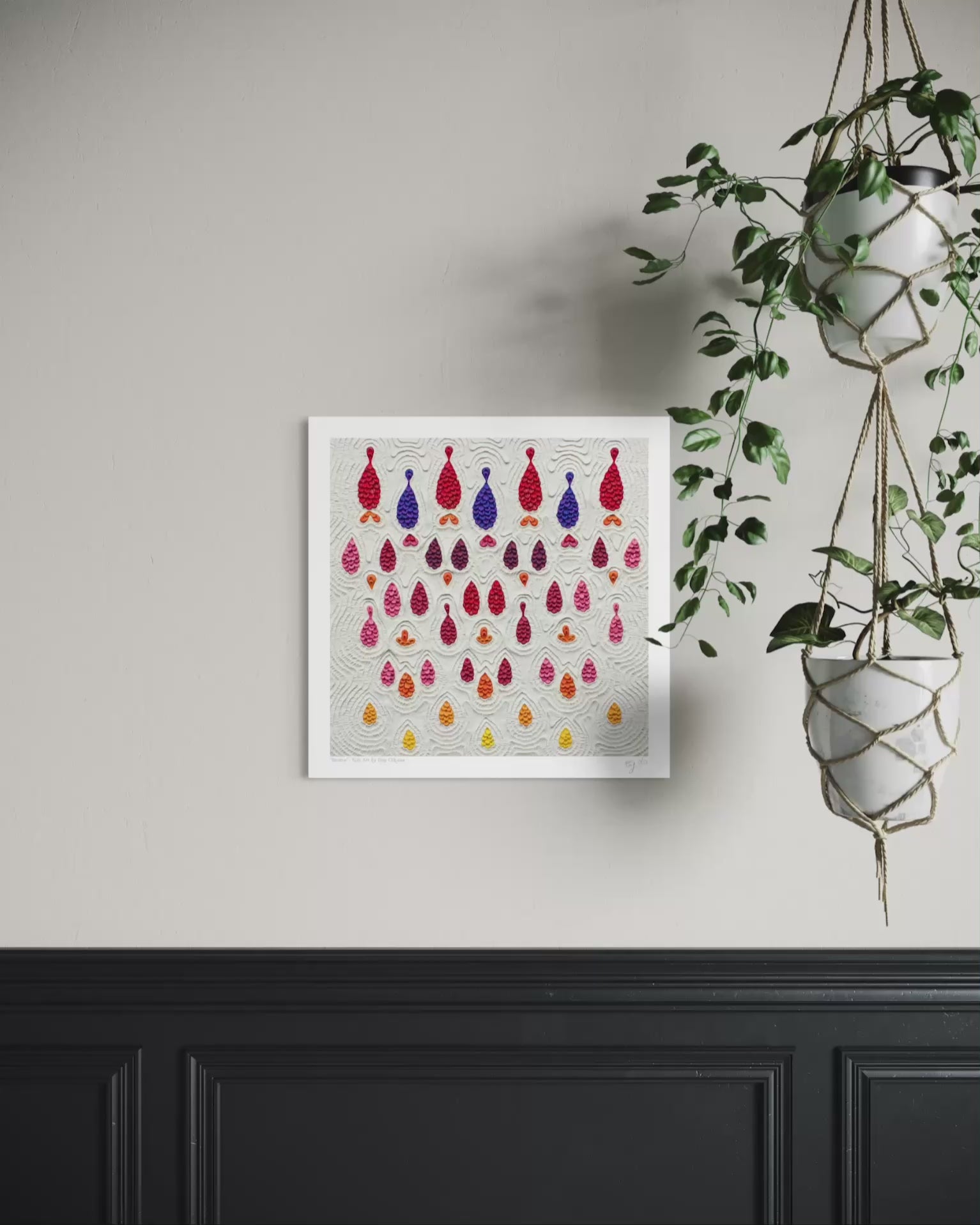 A square wall art print called ''Receive'' featuring rows of colorful hanging teardrop-shaped made with plasticine clay on a light gray background, displayed on a beige wall above a black wainscoted panel with a green hanging plant to the right. Art by New Zealand clay artist Emy Oikawa.