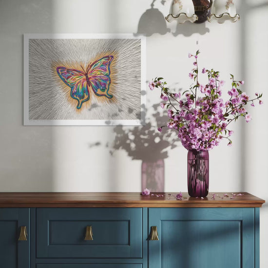 Close up video of an A3 butterfly art print called ''Spirit Sign'' by clay artist Emy Oikawa from Eclo Art, hangs on a white wall above a blue wooden cabinet, with a purple vase of pink blossoms.