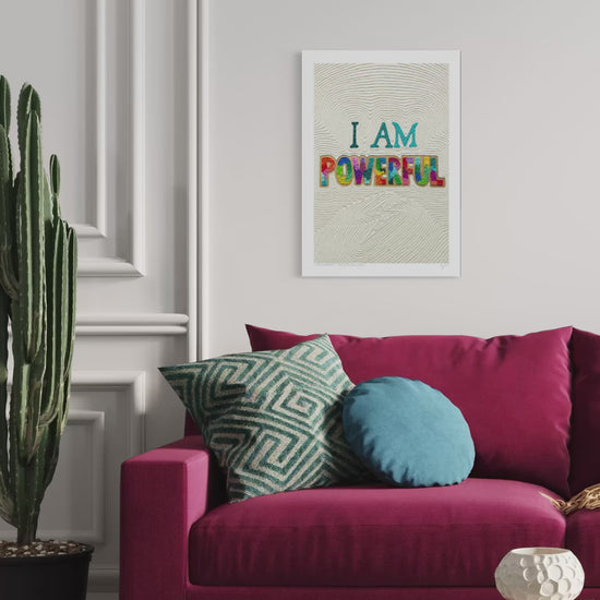 A close up video of a plasticine clay wall art print with the text 'I AM POWERFUL' hangs on a white wall above a magenta sofa with decorative pillows. Positive and empowering art for everyone! Art by New Zealand clay artist Emy Oikawa from Eclo Art.