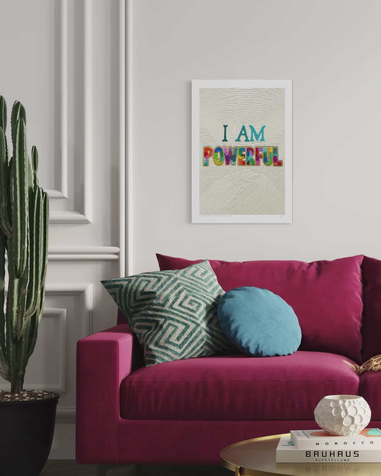 A close up video of a plasticine clay wall art print with the text 'I AM POWERFUL' hangs on a white wall above a magenta sofa with decorative pillows. Positive and empowering art for everyone! Art by New Zealand clay artist Emy Oikawa from Eclo Art.